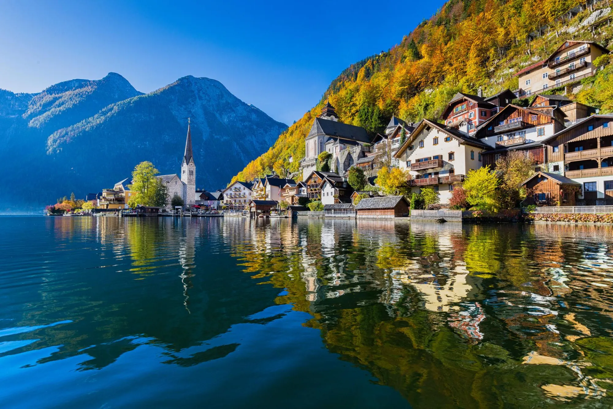 Hallstatt on its alpine lake in autumn, with golden forest on the hillside and the church spire reflected in the water